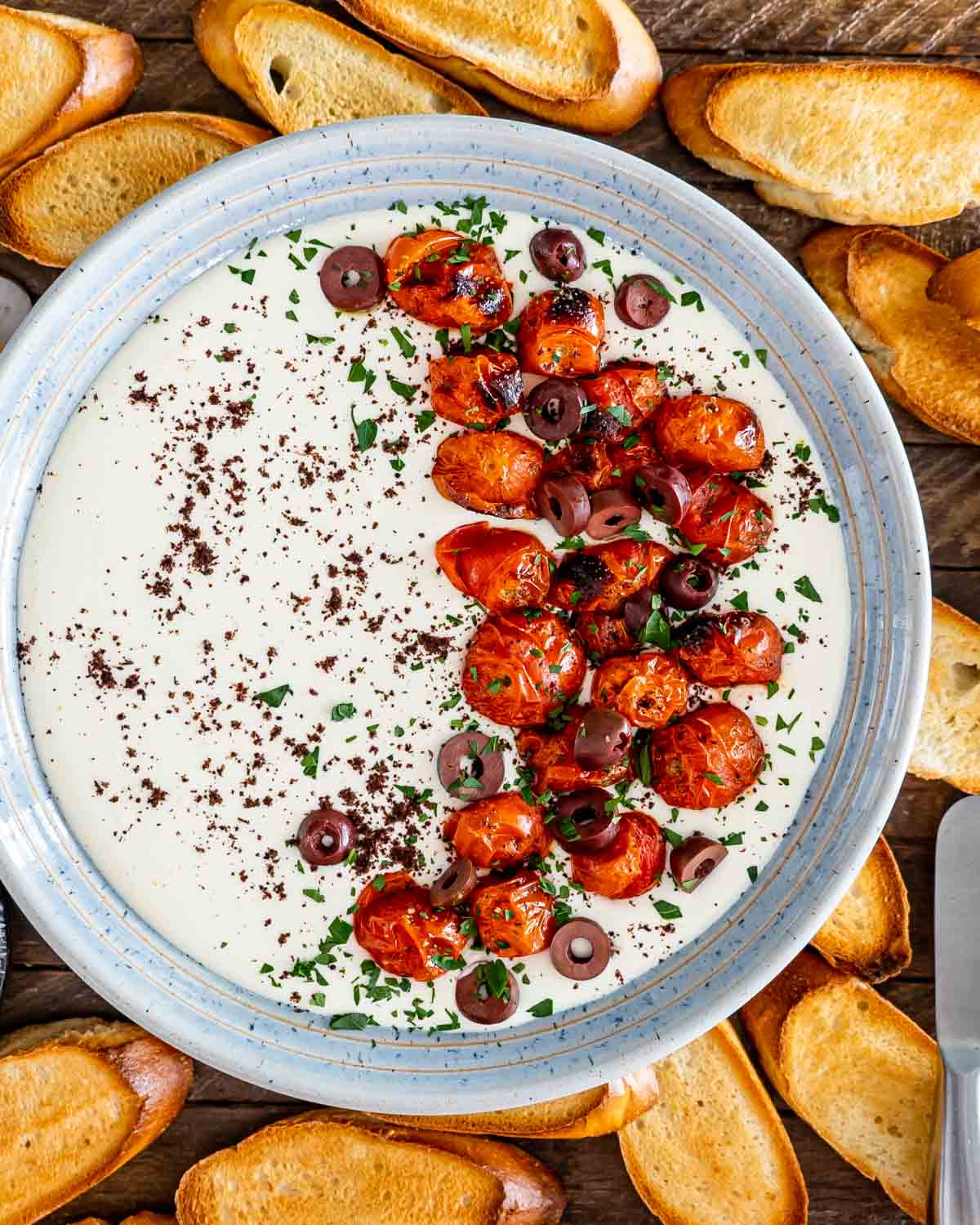 a bowl with whipped feta dip topped with roasted tomatoes surround by pita chips.